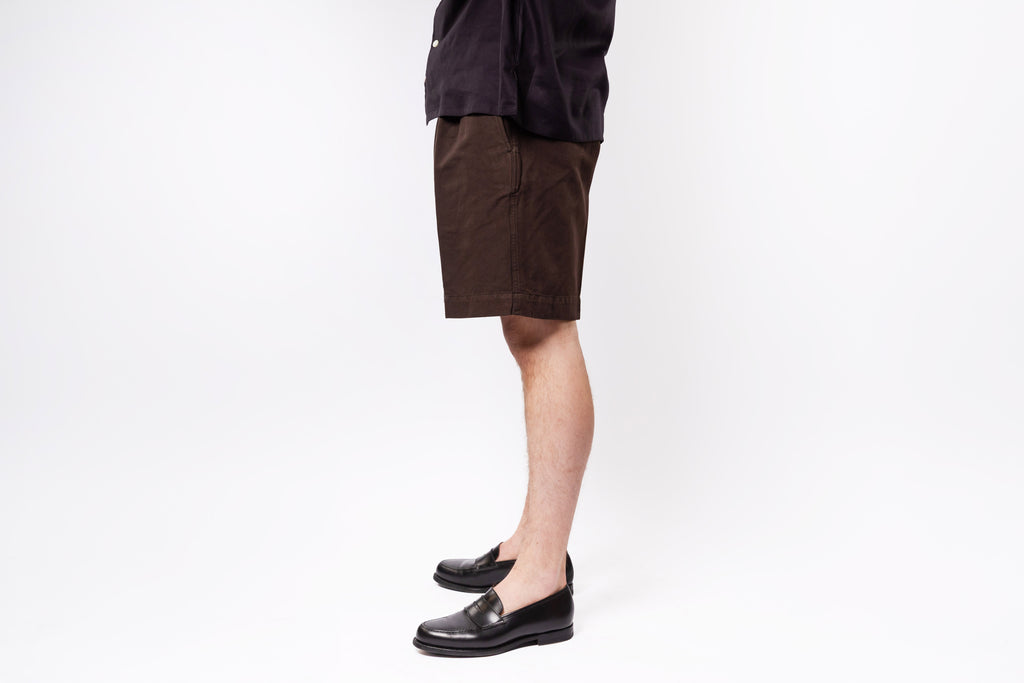 Person wearing brown shorts and black shoes on a white background