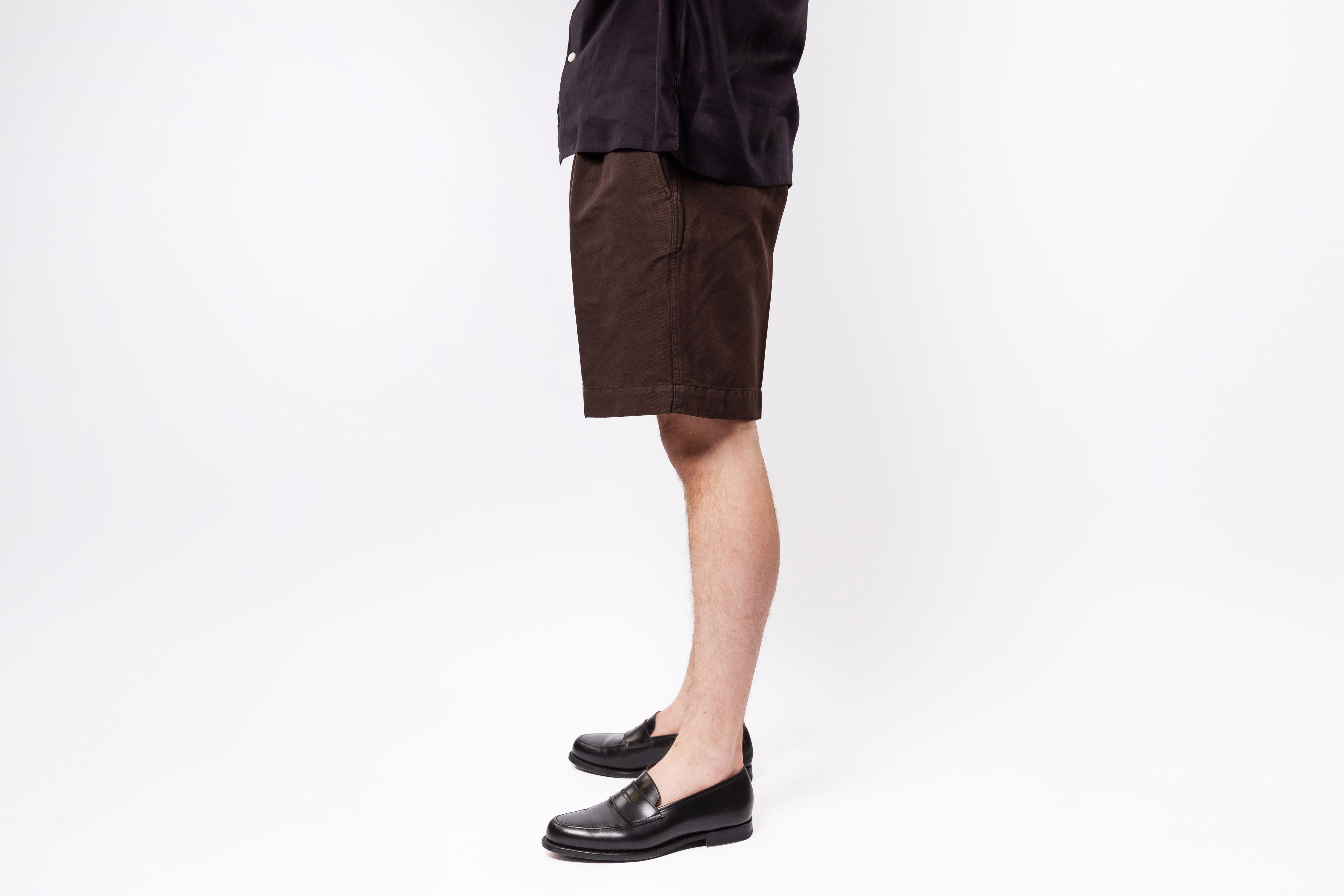Person wearing brown shorts and black shoes on a white background