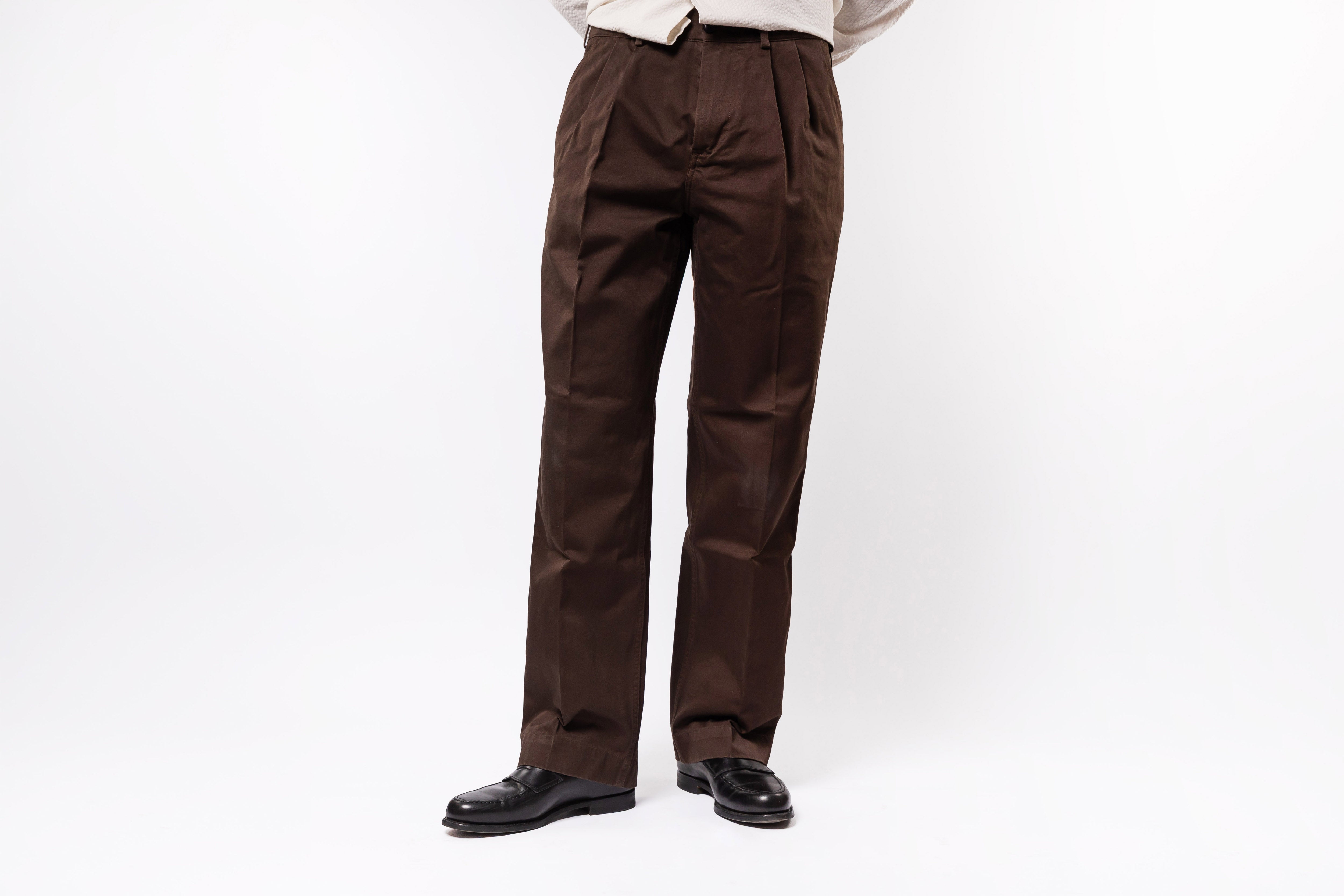 Brown pleated pants worn by a person on a white background