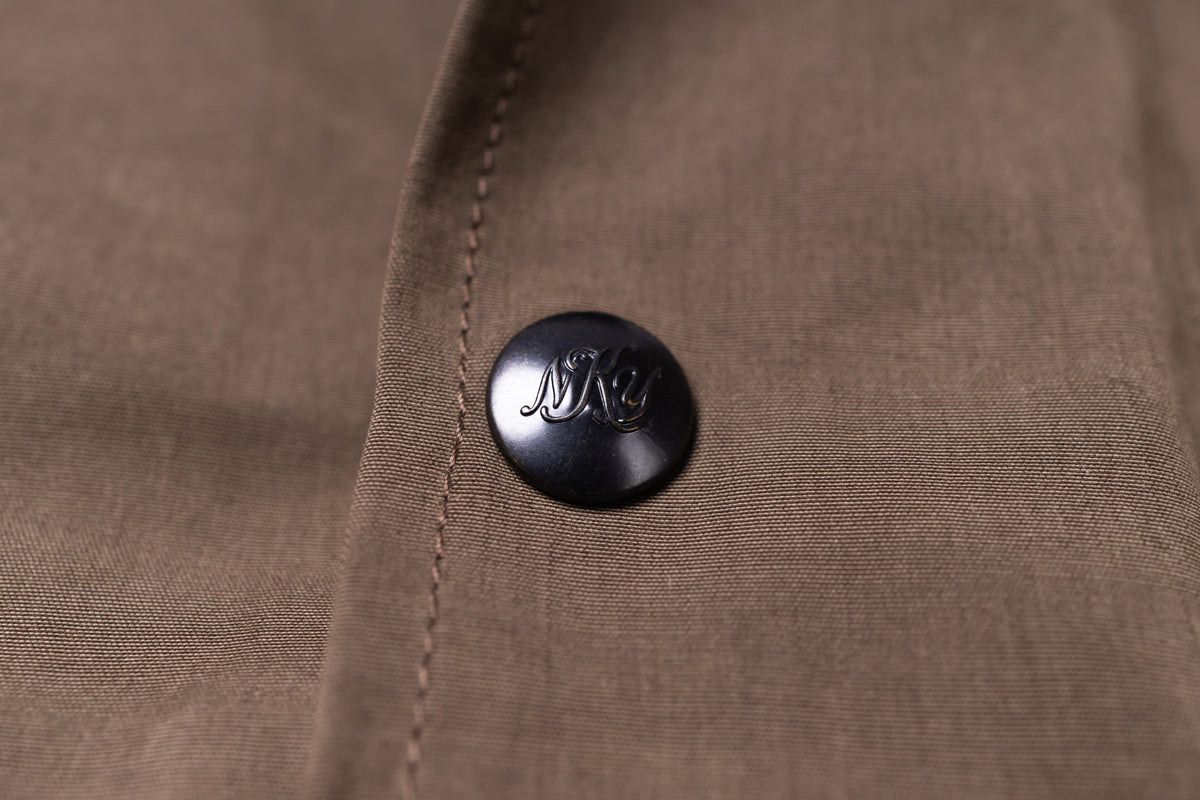 Close-up of a brown textured fabric garment with a black button featuring an embossed stylized 'MNKY logo.