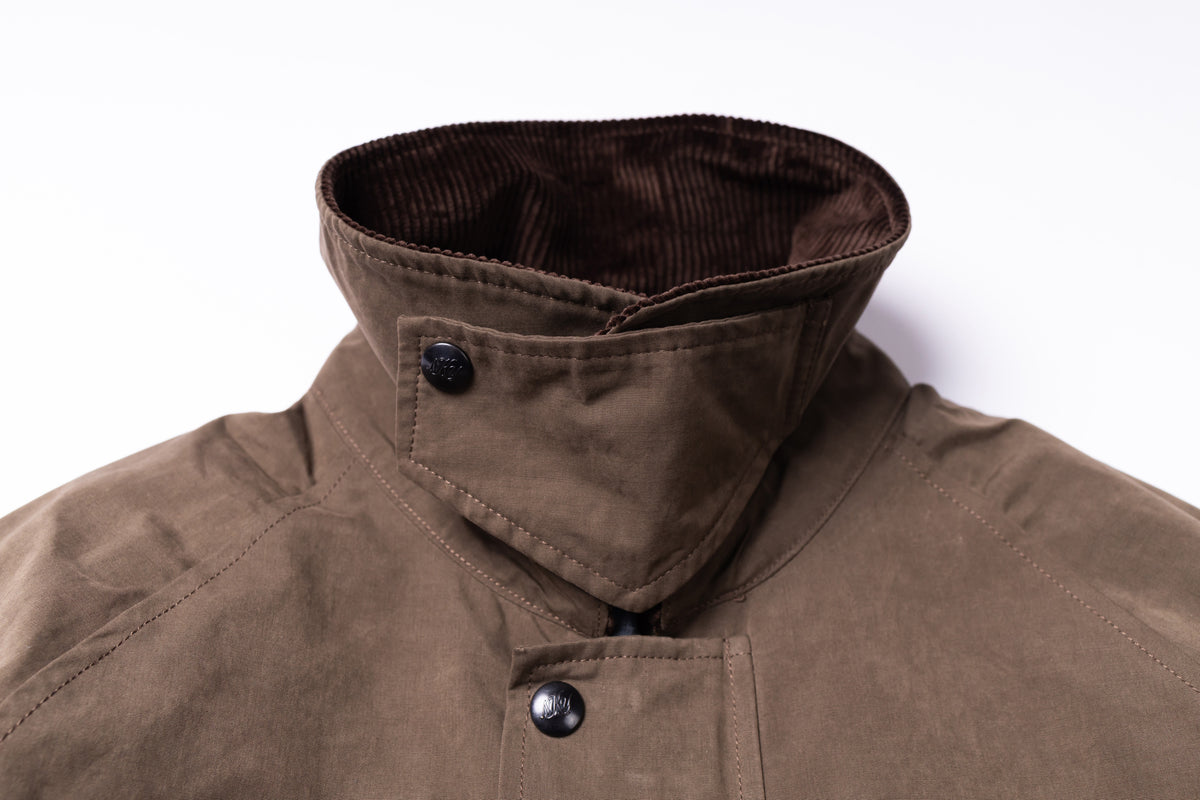 Close-up of a brown corduroy high collar jacket with dark metal snap buttons, shown against a plain white background.