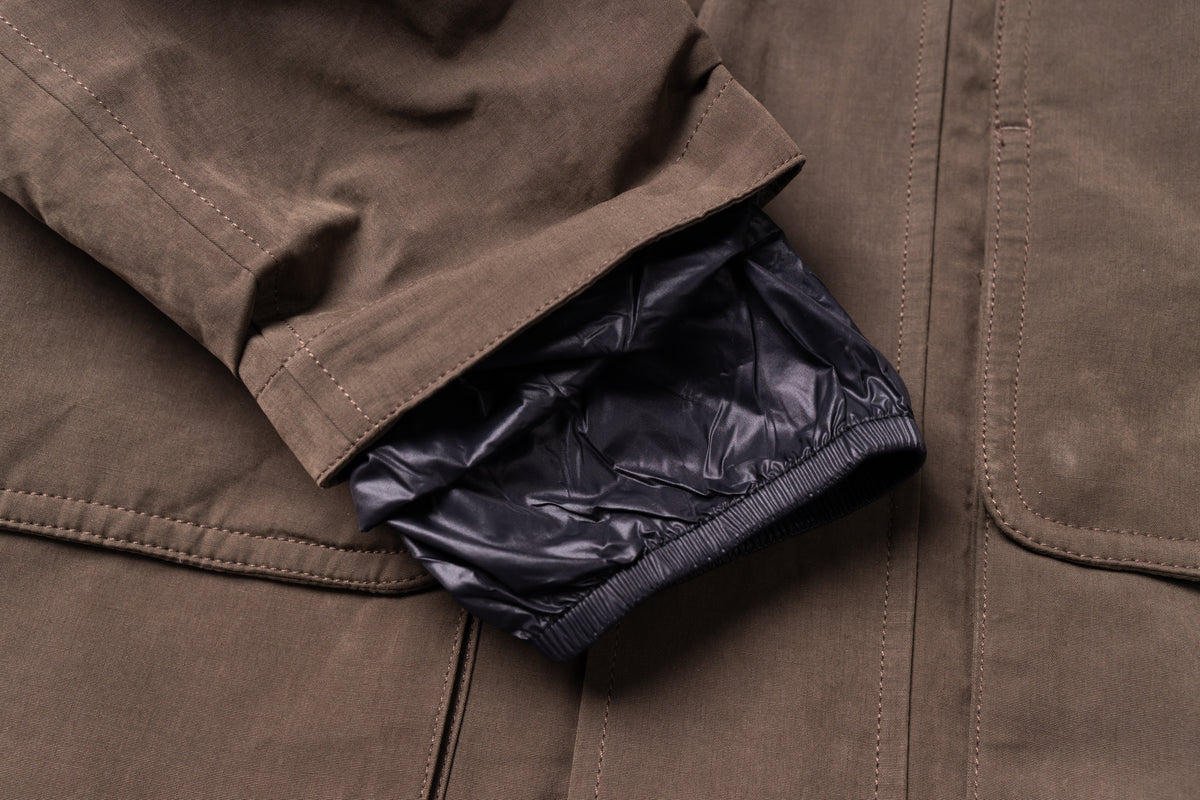 Close-up of a brown jacket sleeve cuff turned up to reveal a shiny black quilted lining.