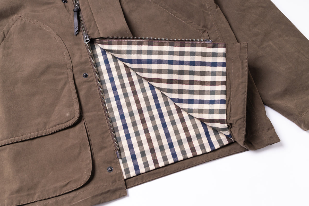 Close-up of a brown jacket with a zippered pocket opening, showing a plaid interior lining in beige, blue, and brown on a white background.