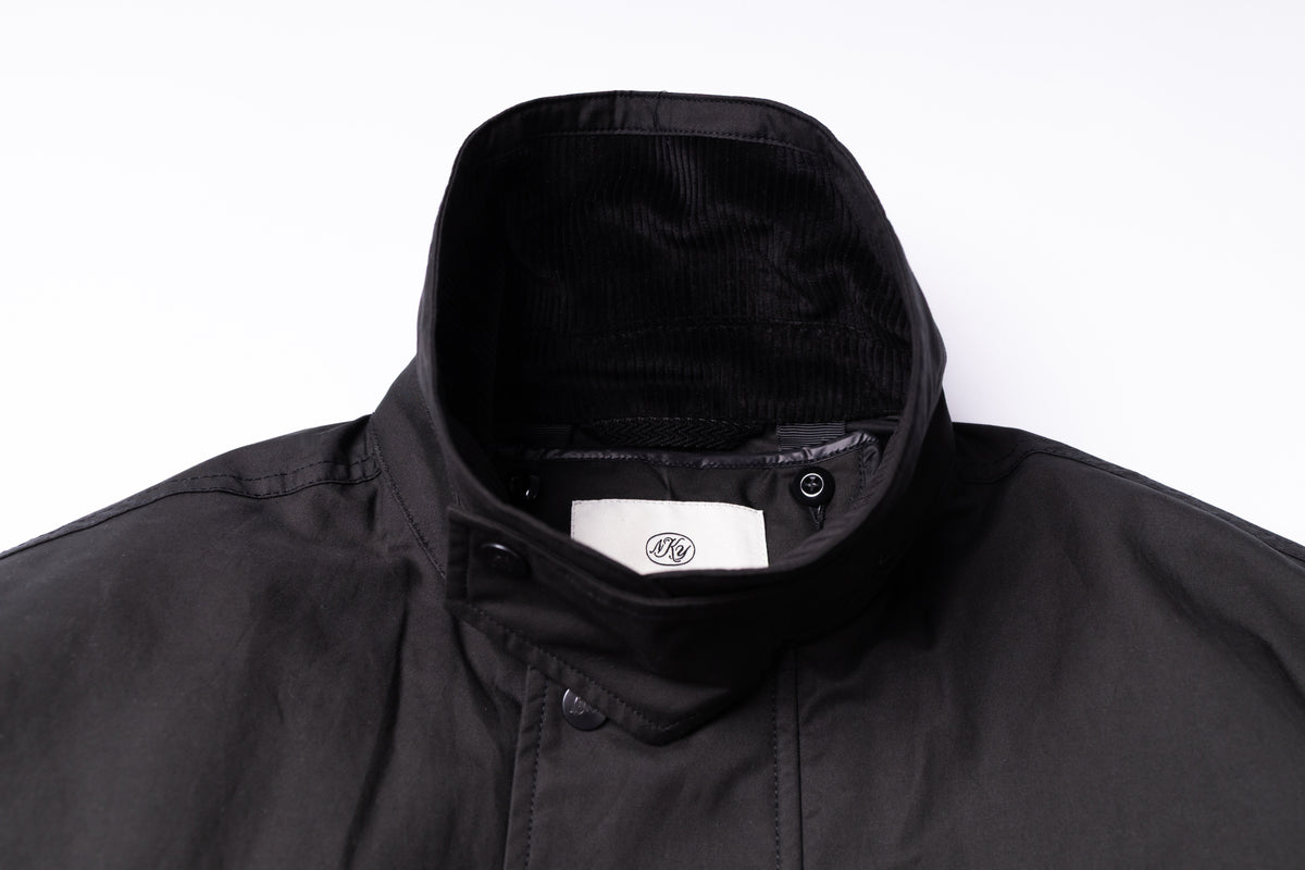 Close-up of a black jacket collar with a white interior label featuring a circular logo, set against a plain white background.