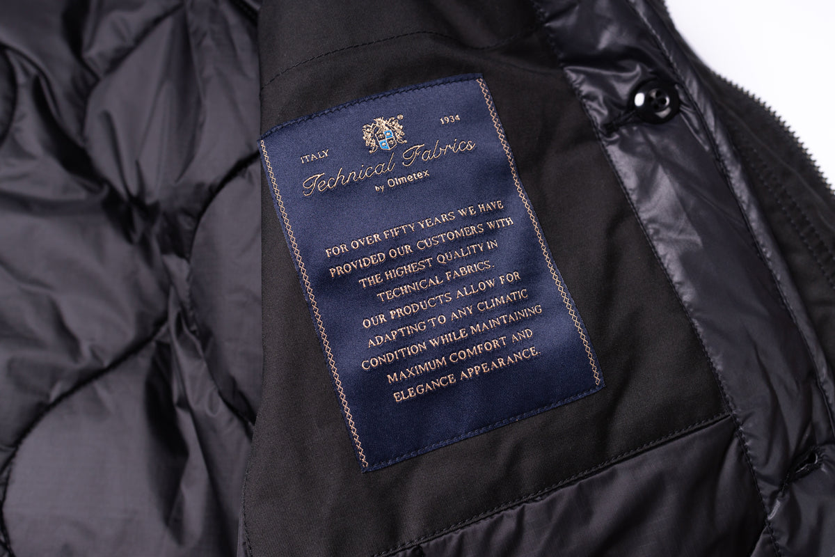 Close-up of a black puffer jacket interior showing a navy blue technical fabric label sewn inside the collar.