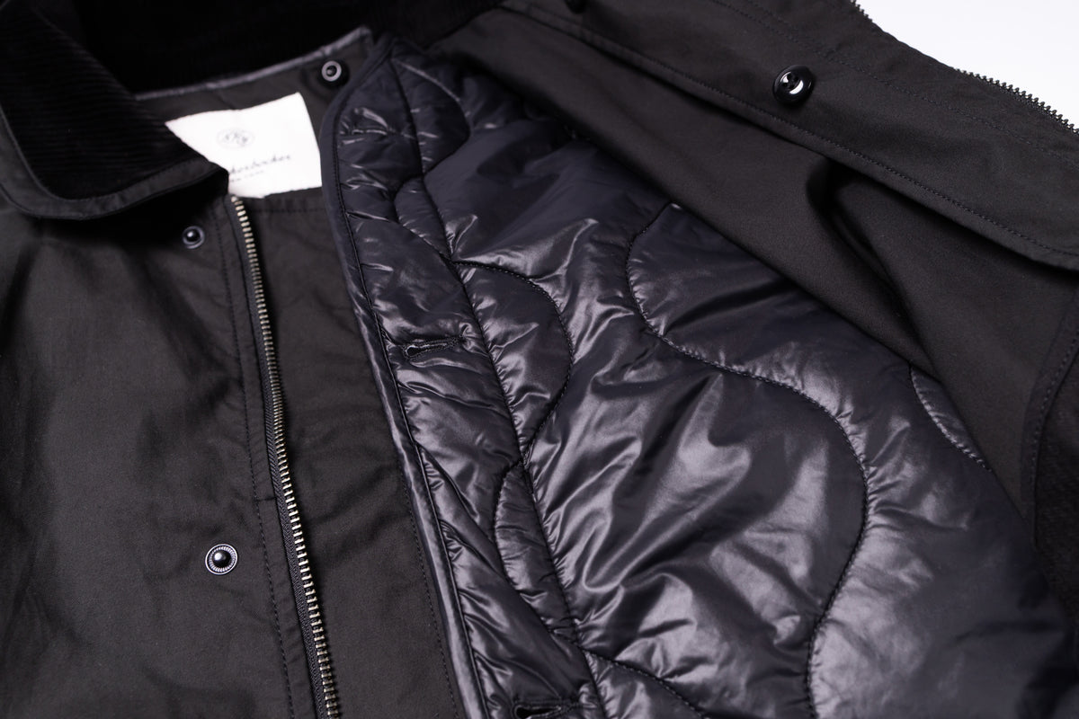 Close-up of a black jacket showing the quilted puffer lining, a black collar, snap buttons, and a zipper on a white background.