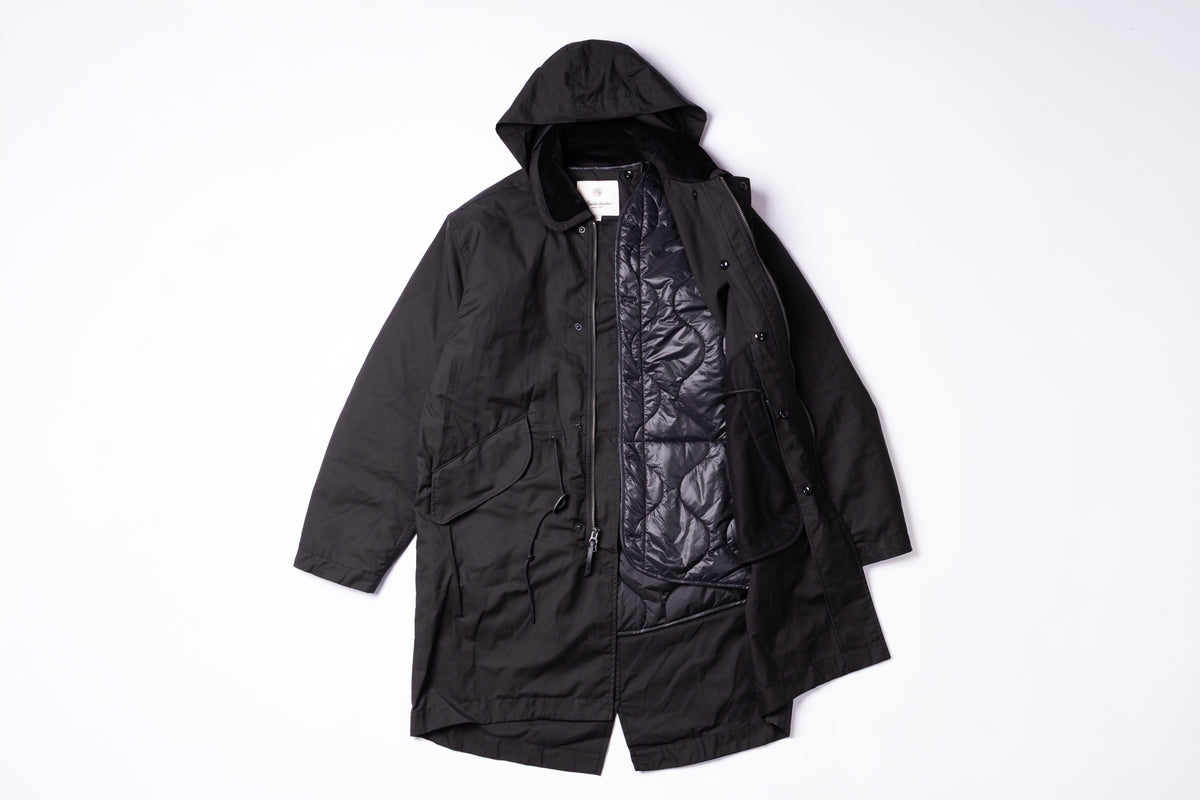 A black hooded utility jacket with front flap pockets, laid flat against a clean white background.