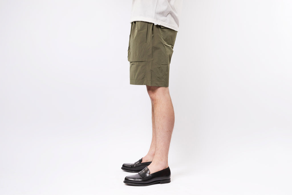 Person wearing olive green shorts and black shoes on a white background