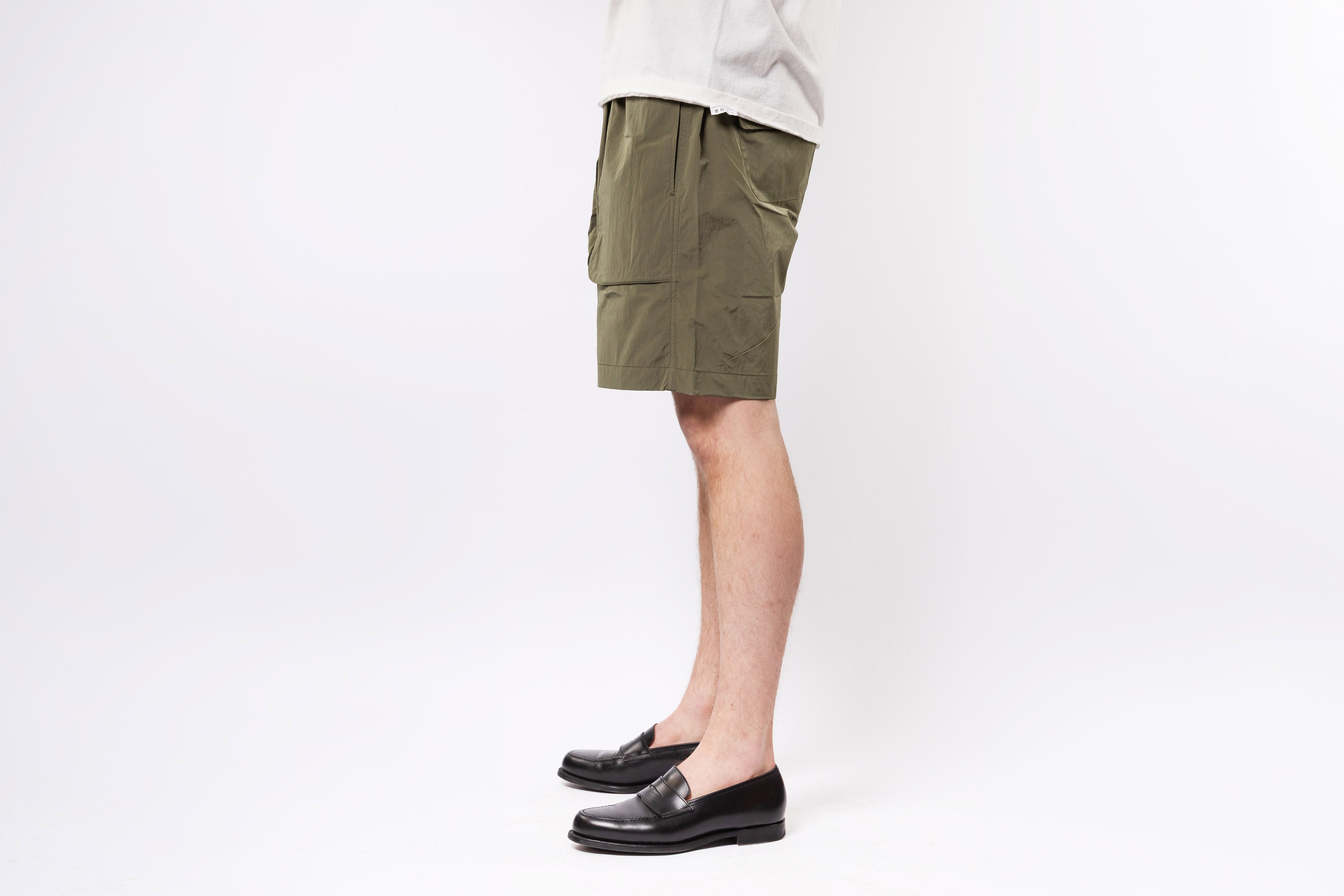 Person wearing olive green shorts and black shoes on a white background