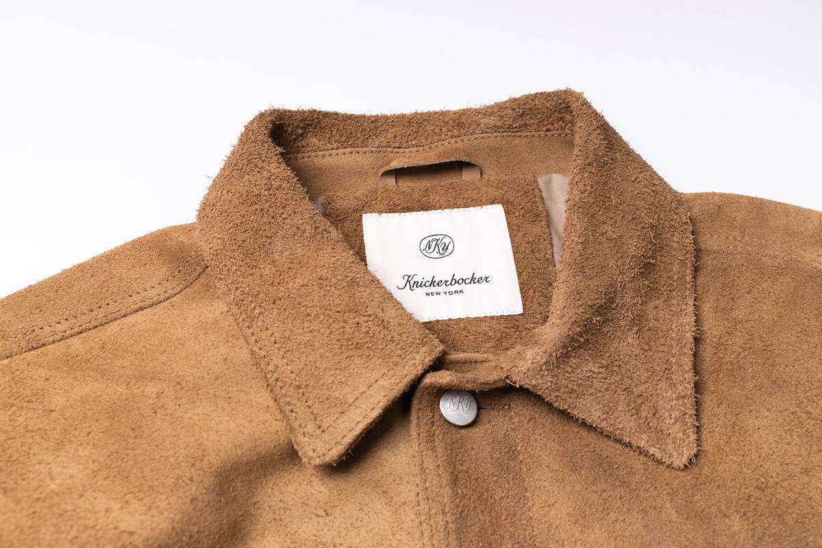 Close-up of a tan suede or nubuck overshirt collar with a white neck label reading 'Knickerbocker' and a silver snap button at the collar.