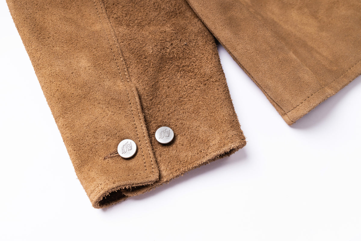 Close-up of a brown suede jacket sleeve with two silver metal snap buttons, shown on a clean white background.