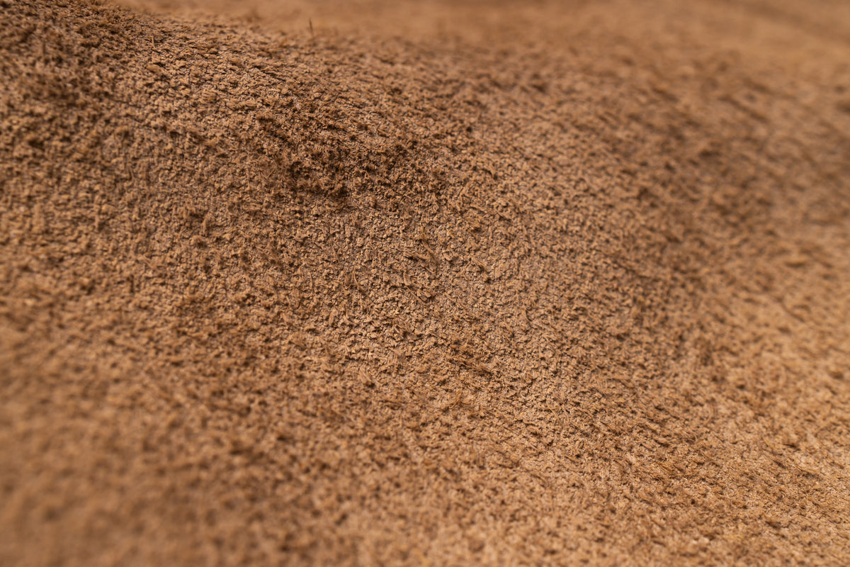 A close-up texture shot of a fine brown powder, such as cocoa powder, coffee grounds, or sand, filling the frame with a shallow depth of field.