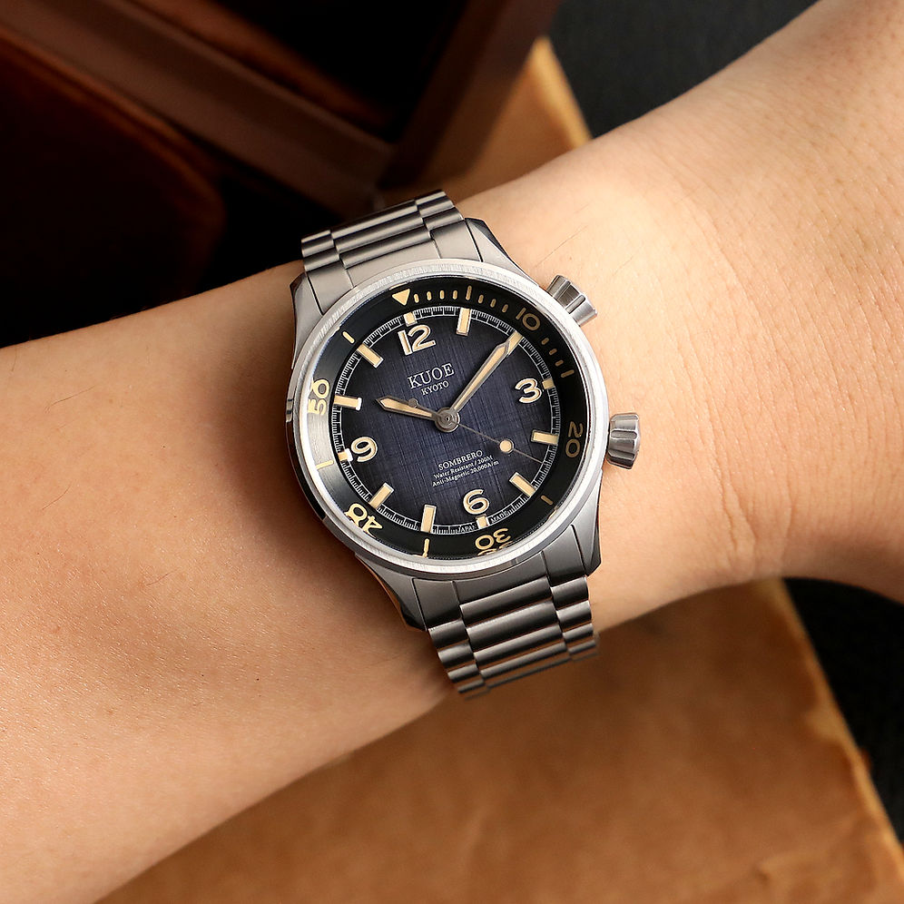 A wristwatch with a stainless steel case and integrated metal bracelet, featuring a dark blue sunburst dial.
