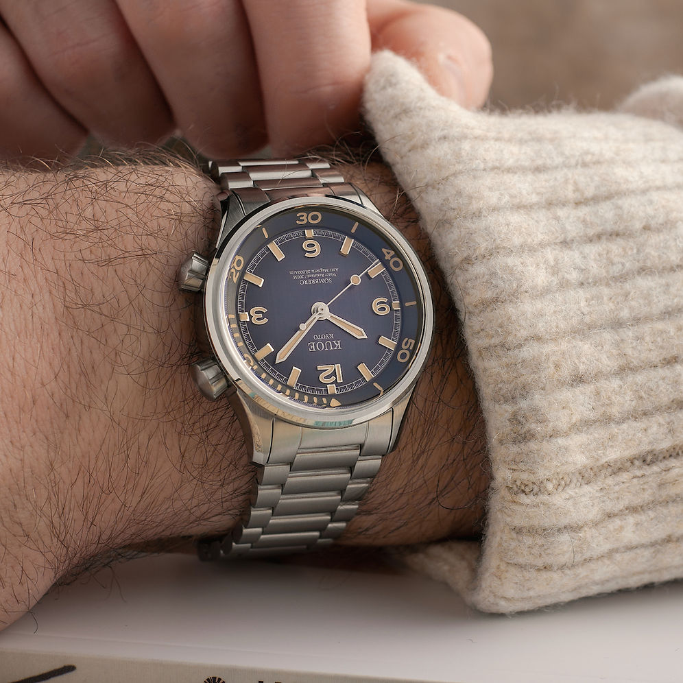 A wristwatch with a dark blue dial and a silver metal bracelet, worn on a person's wrist with a beige knit sweater cuff visible.