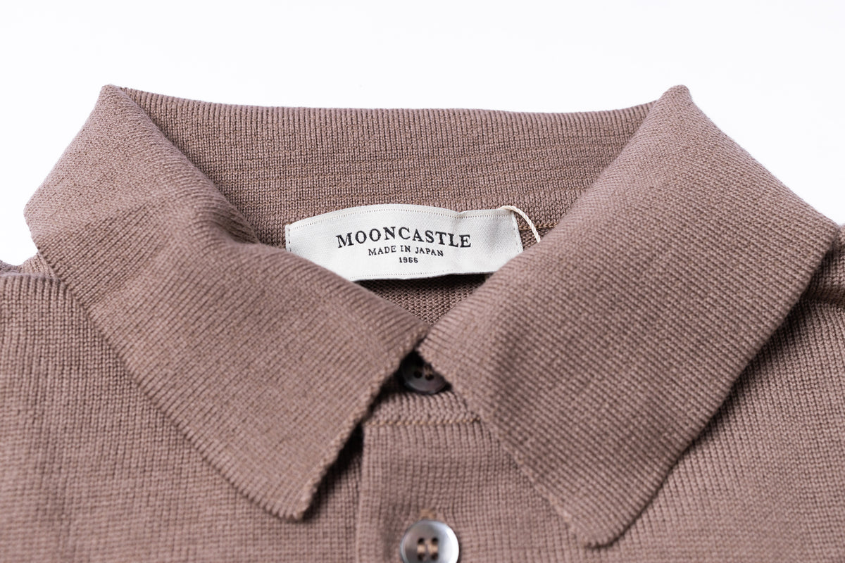 Close-up of a knit polo shirt collar in a muted taupe-brown color, showing a white brand label that reads MOONCASTLE MADE IN JAPAN 1995.