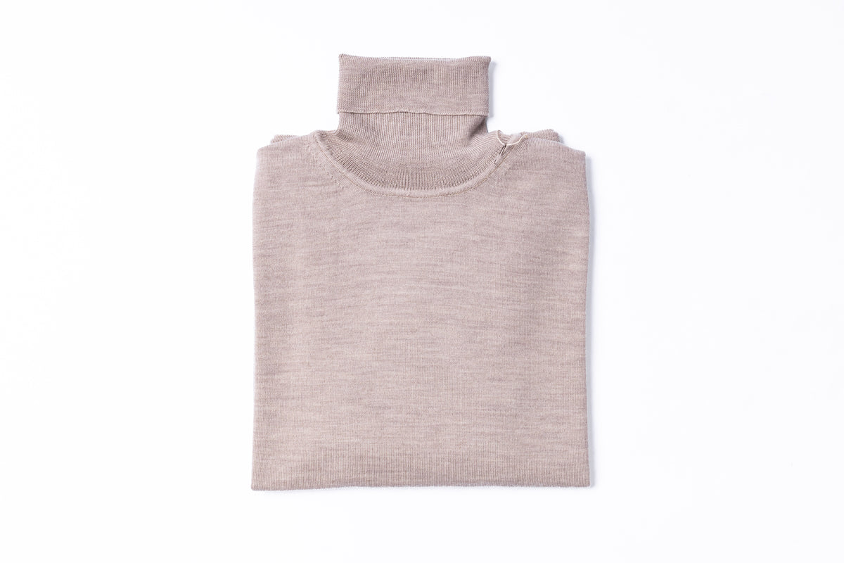 A folded knit turtleneck sweater in a light taupe-beige color, presented flat against a solid white background.