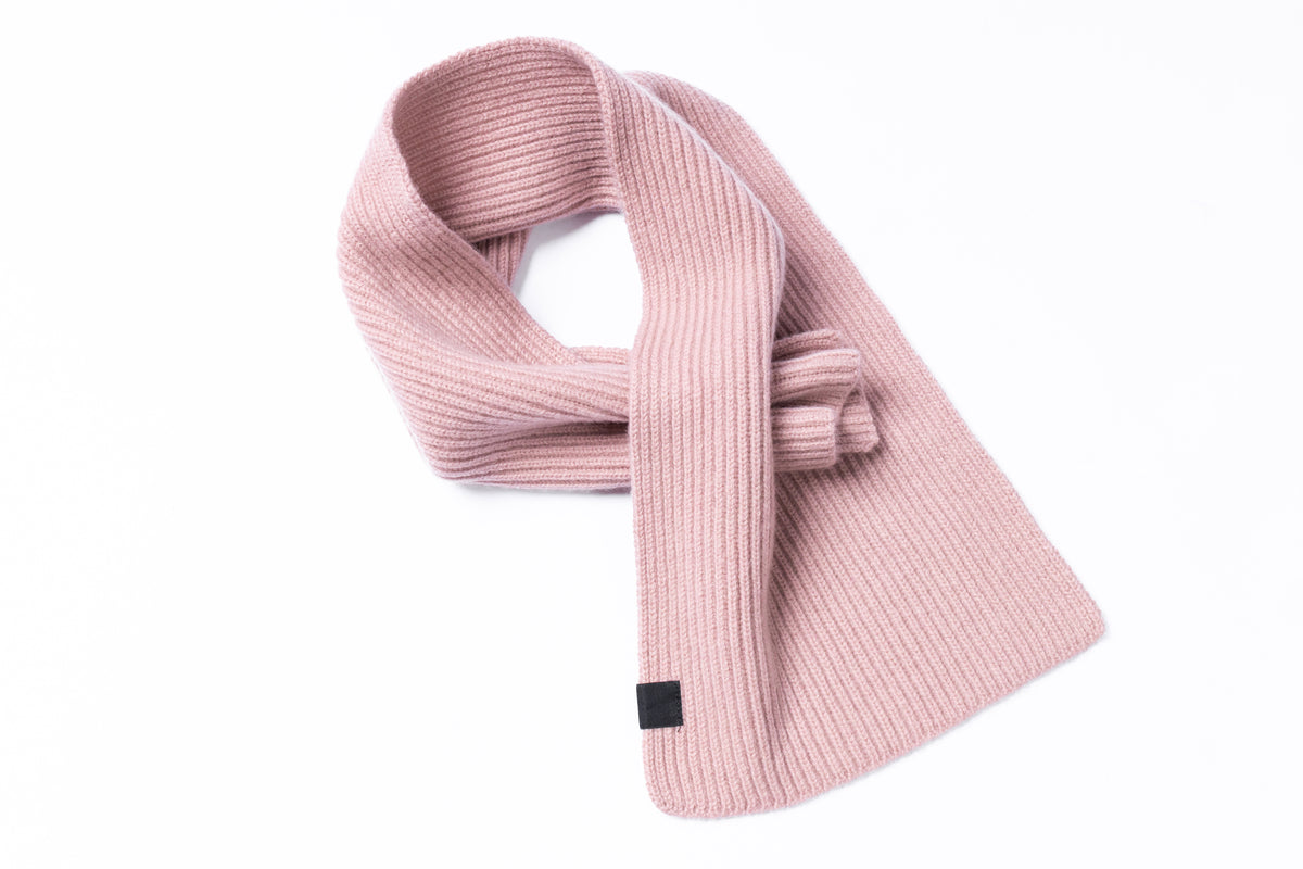 A dusty pink ribbed knit scarf with a small black square tag, styled in a loop on a clean white background.