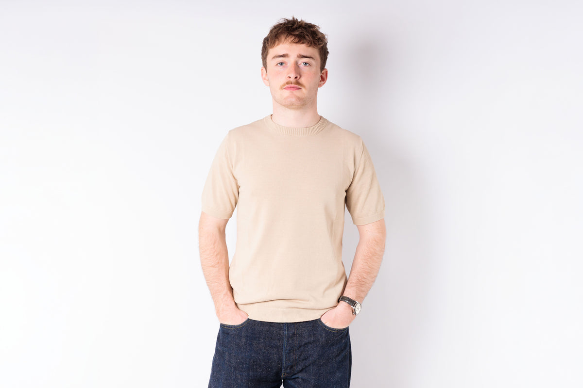 Person wearing a beige sweater and dark pants on a white background