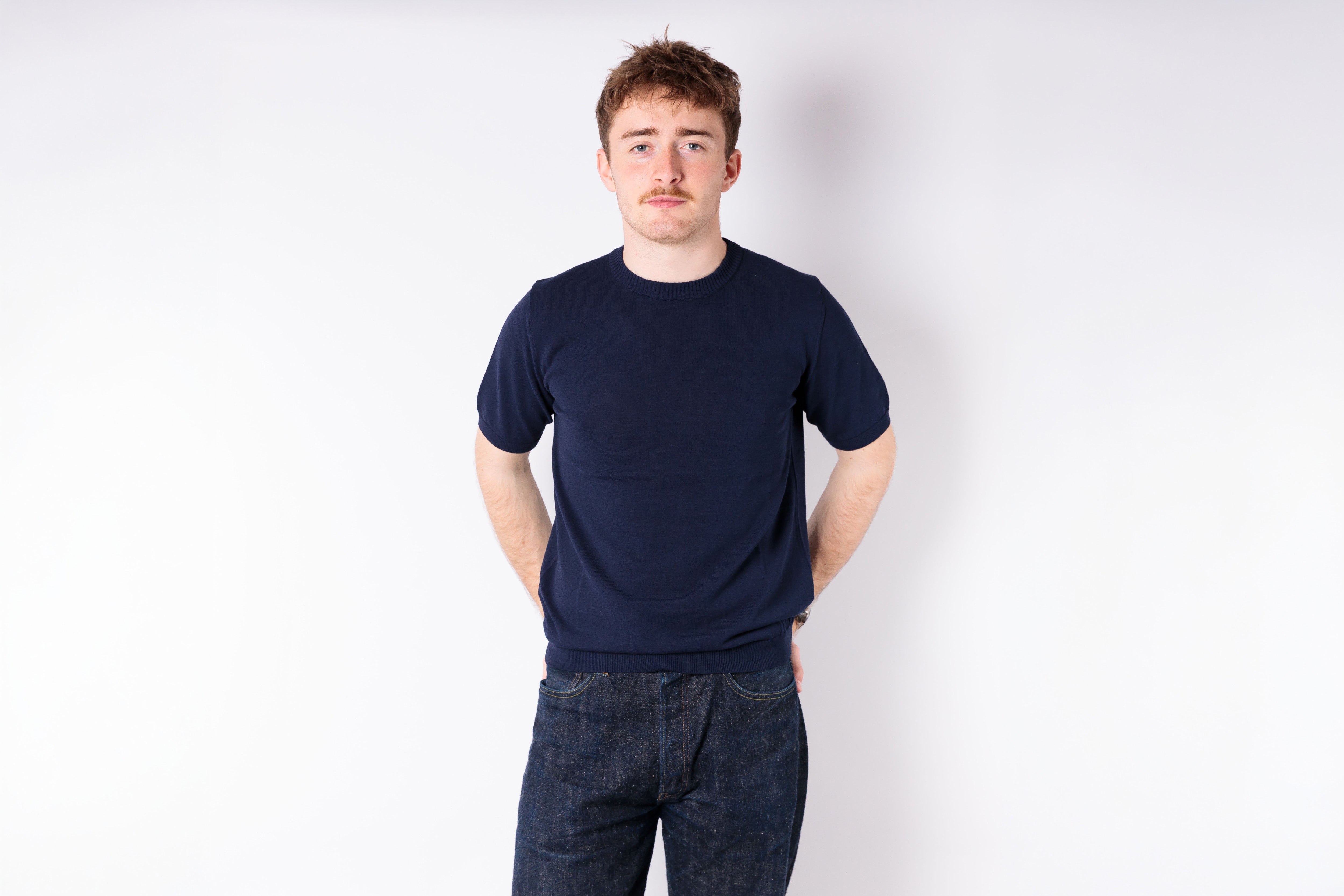 Man wearing a navy blue t-shirt and jeans against a white background