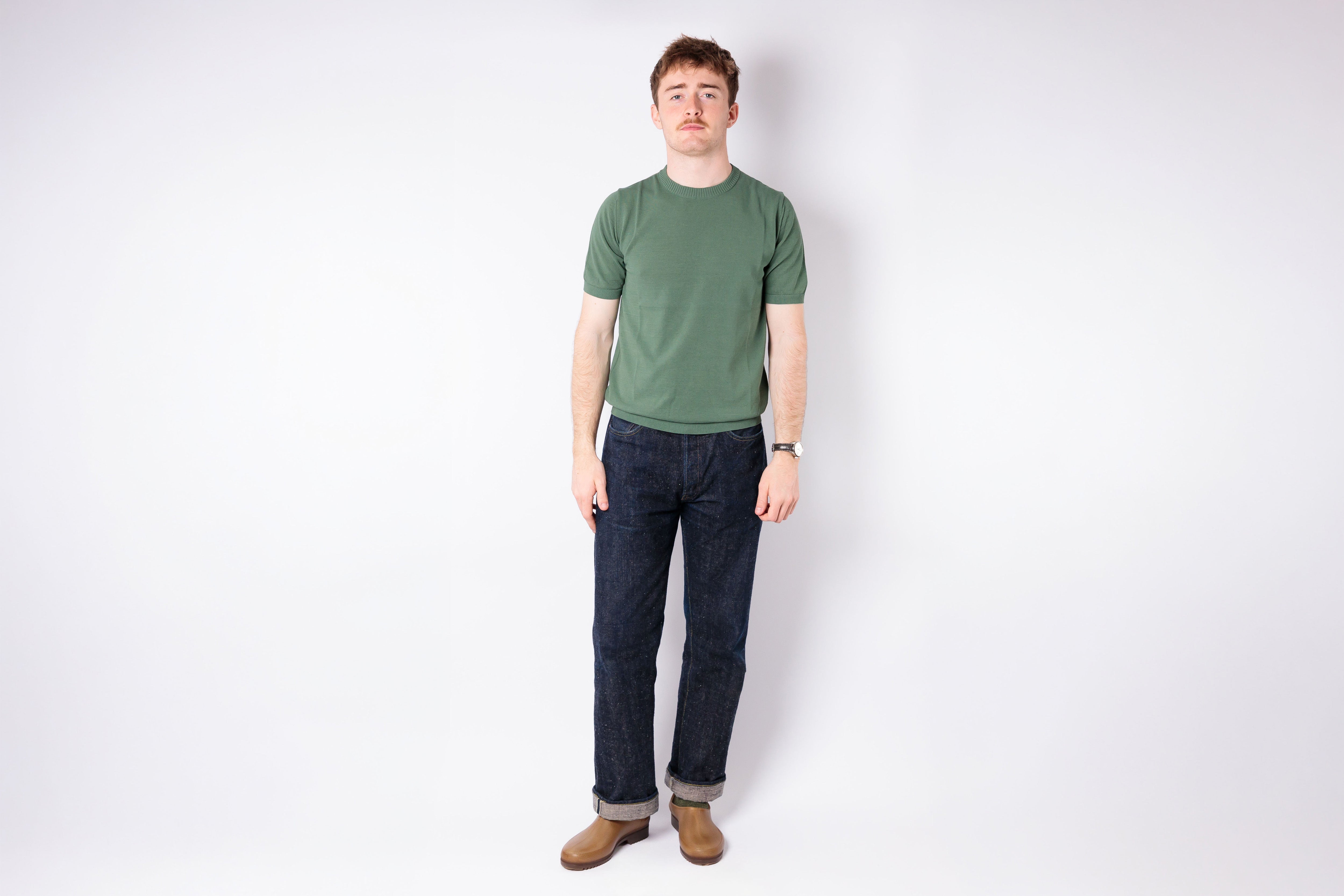 Man wearing a green t-shirt and blue jeans standing against a white background