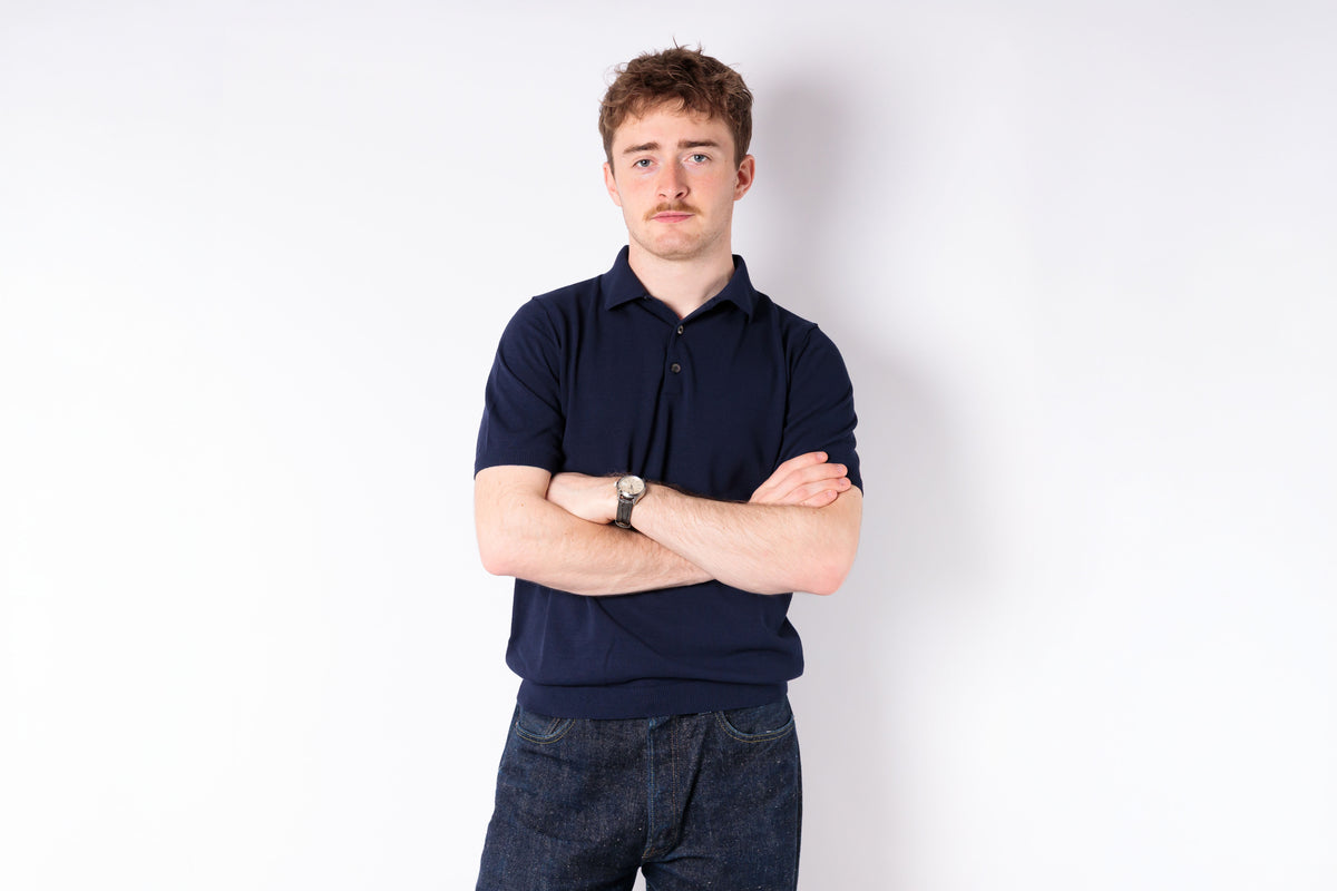 Man wearing a navy blue polo shirt and jeans against a white background