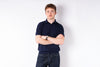 Man wearing a navy blue polo shirt and jeans against a white background