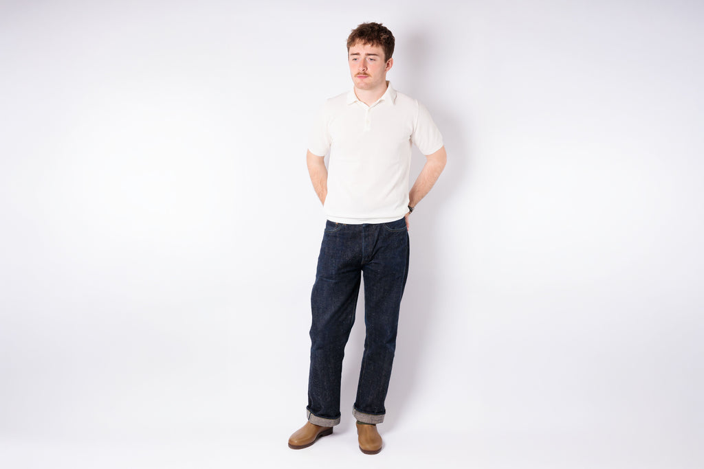 Man wearing a white shirt and dark jeans standing against a plain white background
