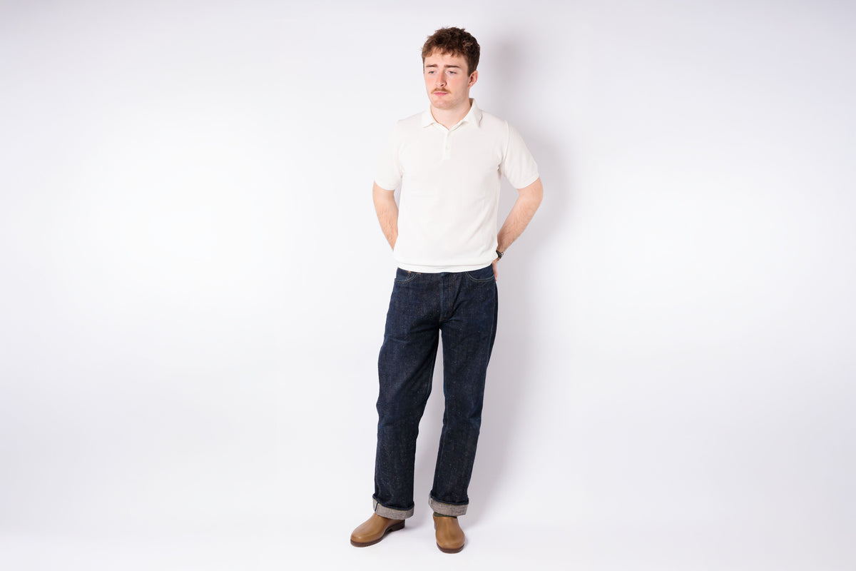 Man wearing a white shirt and dark jeans standing against a plain white background