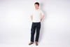 Man wearing a white shirt and dark jeans standing against a plain white background