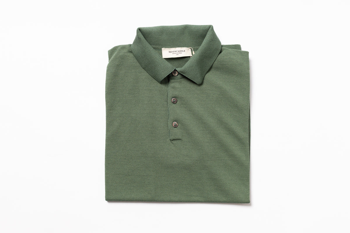 Folded green polo shirt with a brand label on a white background