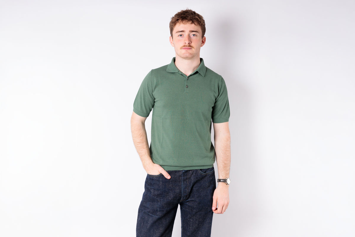 Man wearing a green polo shirt and dark jeans on a white background