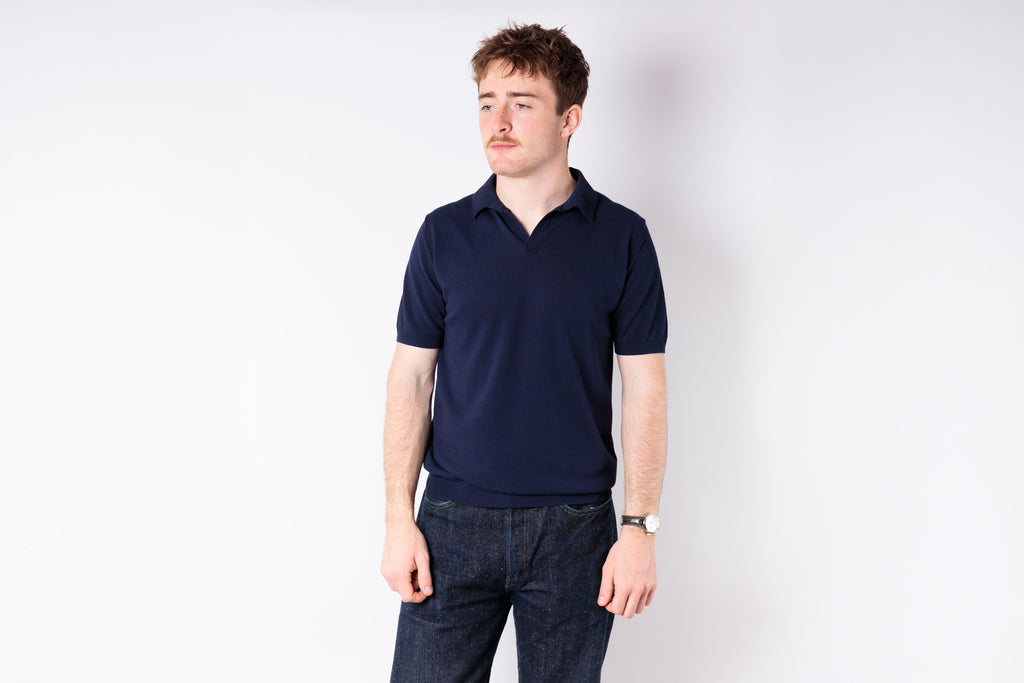 Man wearing a navy polo shirt and jeans on a white background