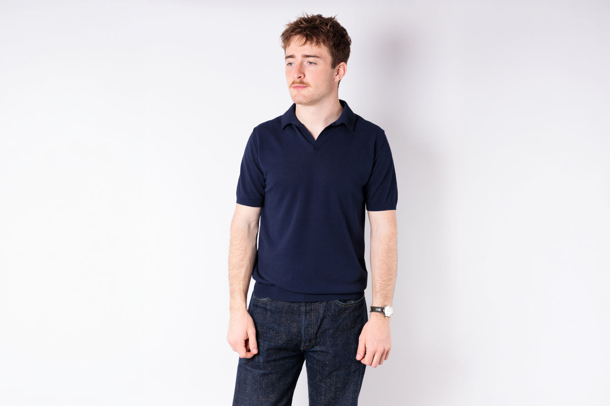 Man wearing a navy polo shirt and jeans on a white background