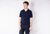 Man wearing a navy polo shirt and jeans on a white background