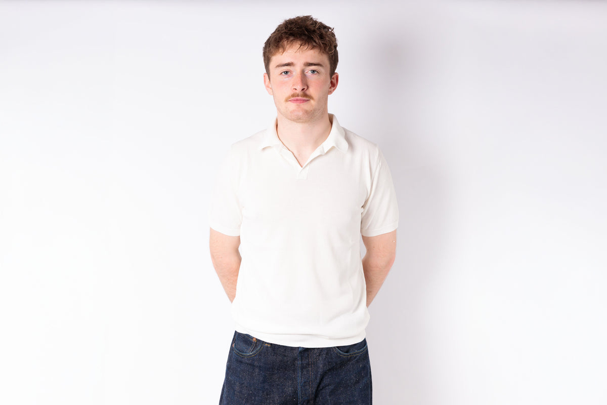 Man wearing a white polo shirt and dark jeans against a white background