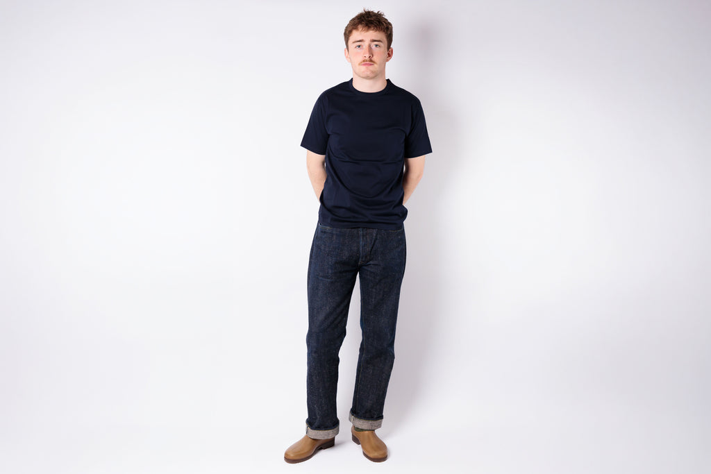 Person wearing a black t-shirt and blue jeans standing against a white background