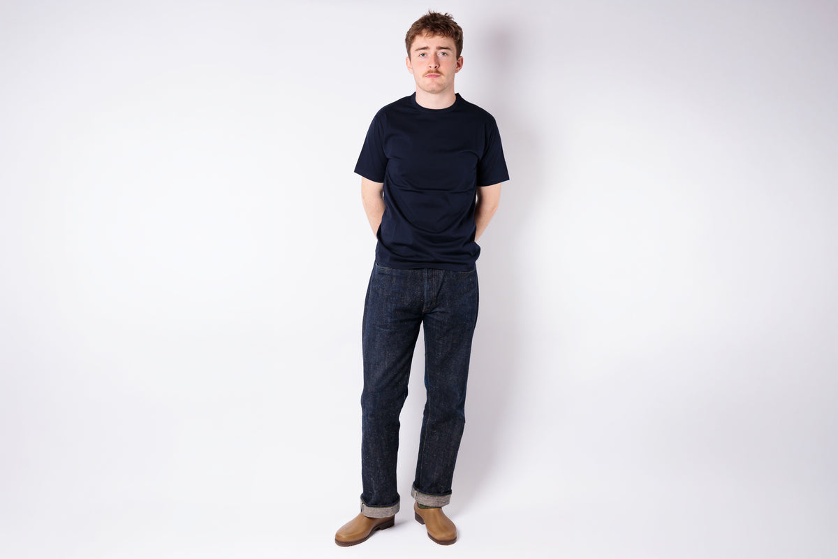 Person wearing a black t-shirt and blue jeans standing against a white background