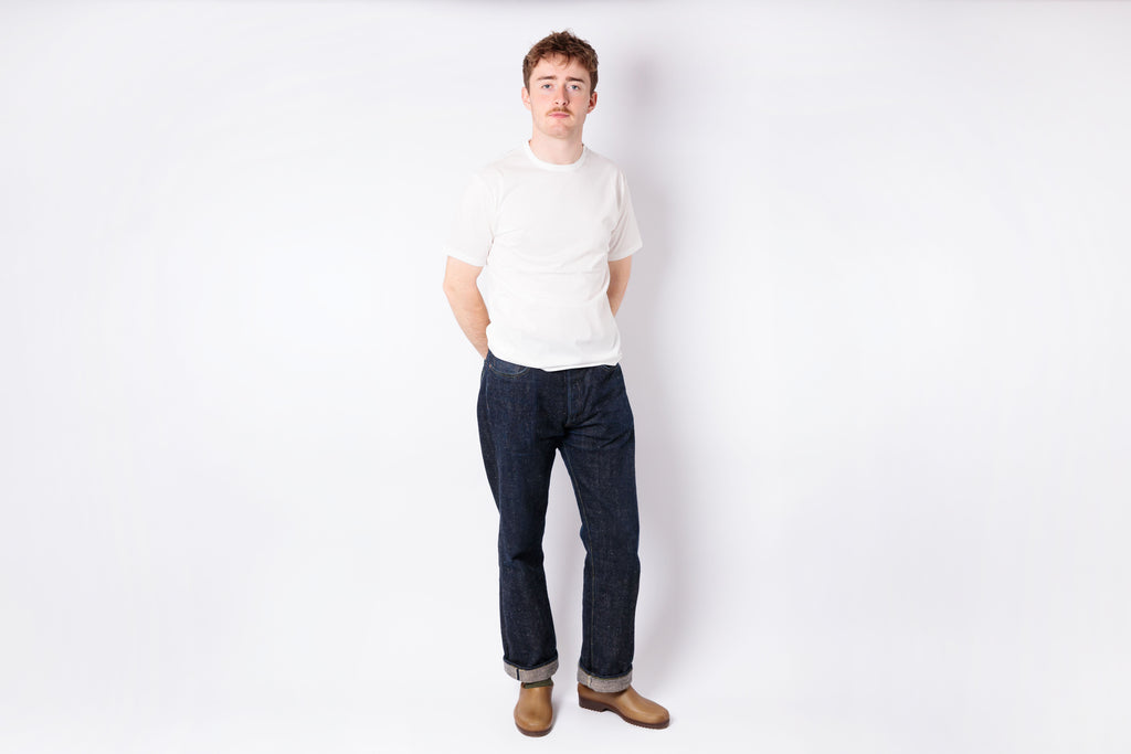 Person wearing a white shirt and dark jeans standing against a plain white background