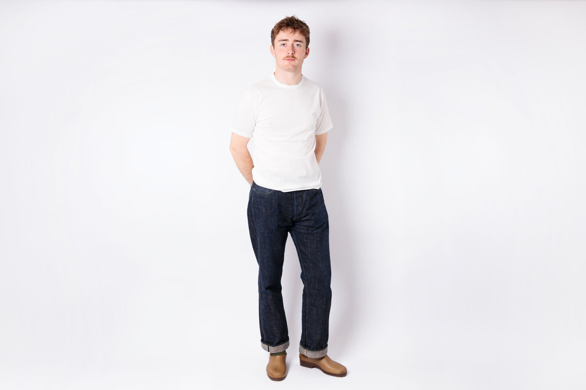 Person wearing a white shirt and dark jeans standing against a plain white background