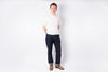 Person wearing a white shirt and dark jeans standing against a plain white background
