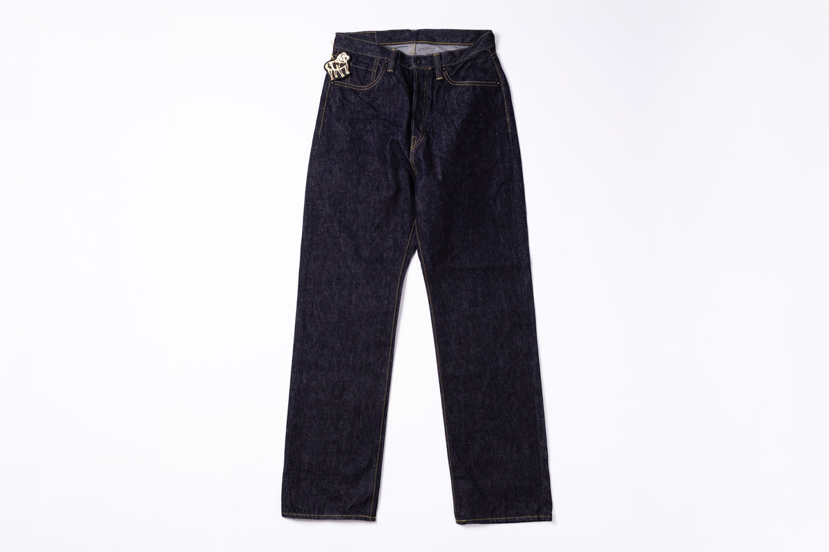 Dark indigo denim jeans with a distinctive silver-toned metal rivet detail on the right hip, laid flat against a white background.