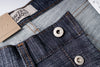 Close-up of denim fabric with button and 'Naked & Famous' label.