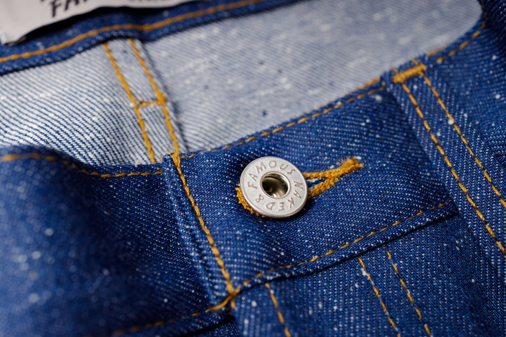 Close-up of a button on blue denim fabric with branding.