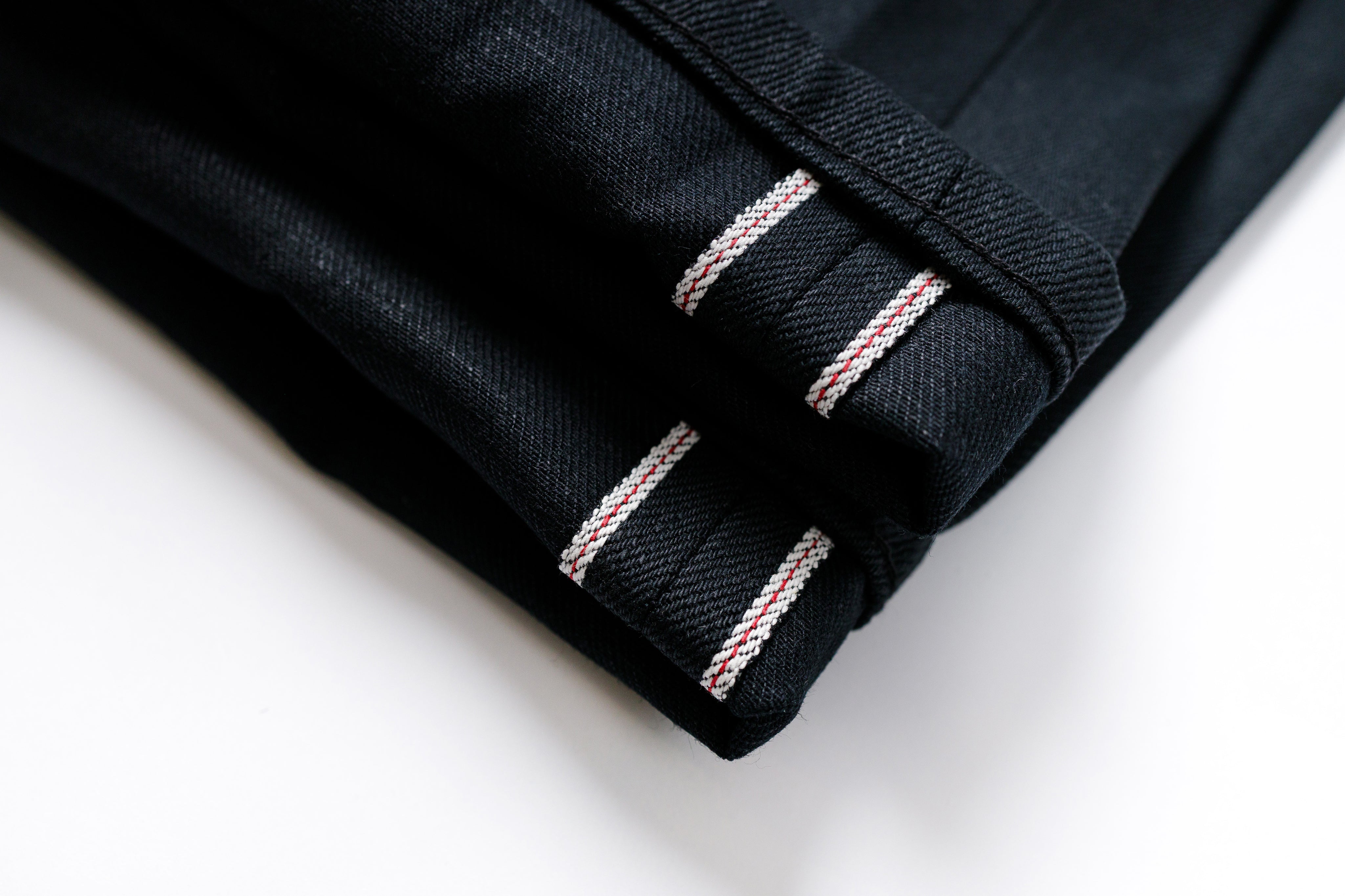 Close-up of black fabric with red and white stitching on a white background