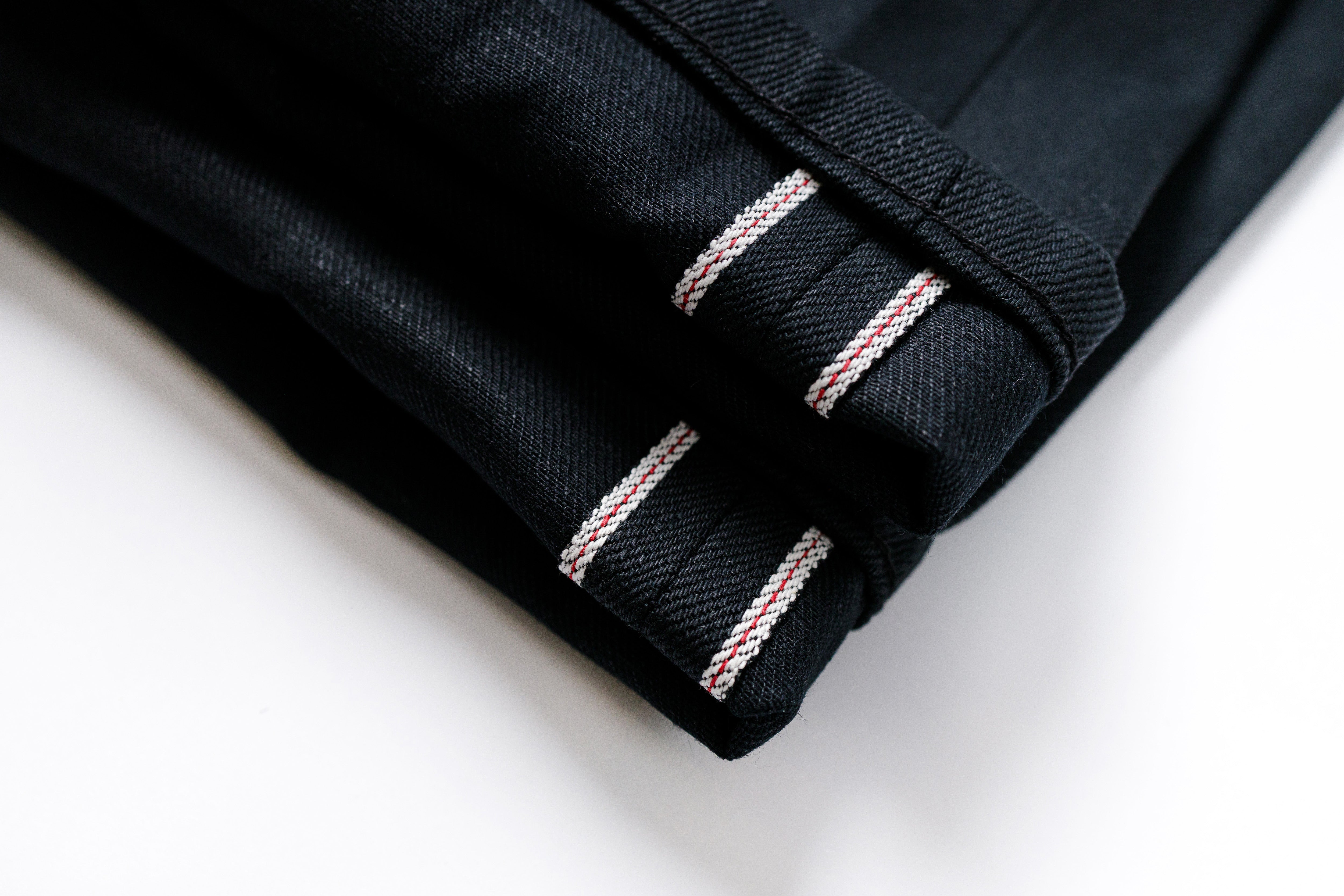 Close-up of black fabric with red and white stitching on a white background