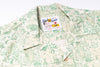 A close-up of a short-sleeve button-up shirt with a light beige and green botanical pattern, featuring a visible 'Natural & Famous' brand label.