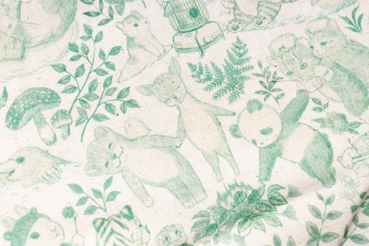 A close-up of a fabric or wallpaper pattern featuring green line-art illustrations of bears, pandas, mushrooms, and leaves on a warm off-white background.