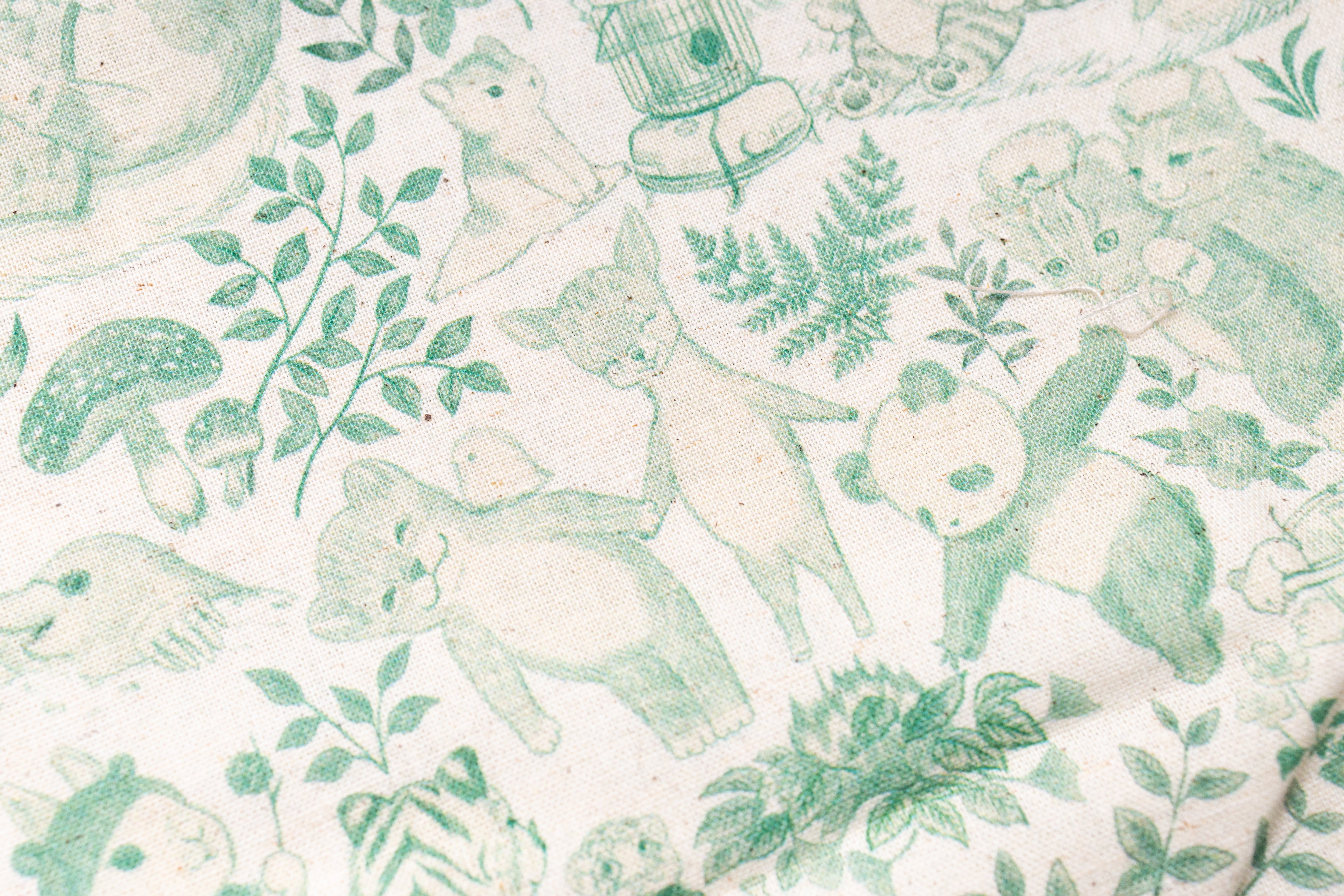 A close-up of a fabric or wallpaper pattern featuring green line-art illustrations of bears, pandas, mushrooms, and leaves on a warm off-white background.