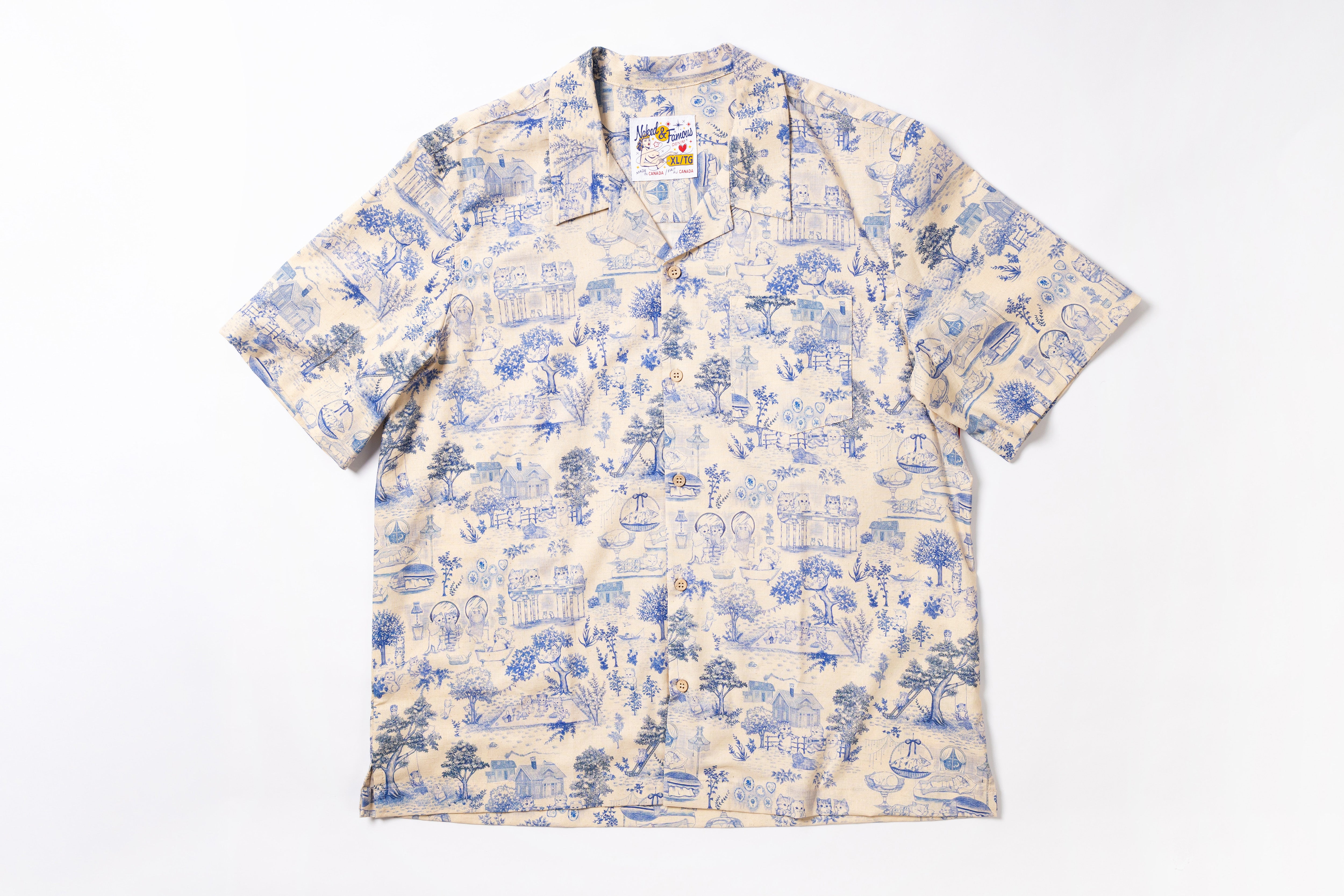 A short-sleeve camp collar button-up shirt with an all-over blue toile-style print on a cream background, laid flat against a white background.