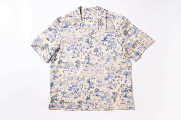 A short-sleeve camp collar button-up shirt with an all-over blue toile-style print on a cream background, laid flat against a white background.